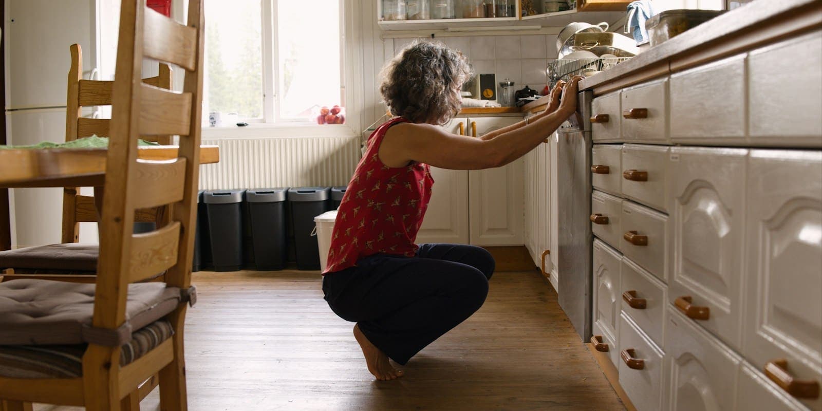Personne accroupie devant son lave-vaisselle pour vérifier une panne